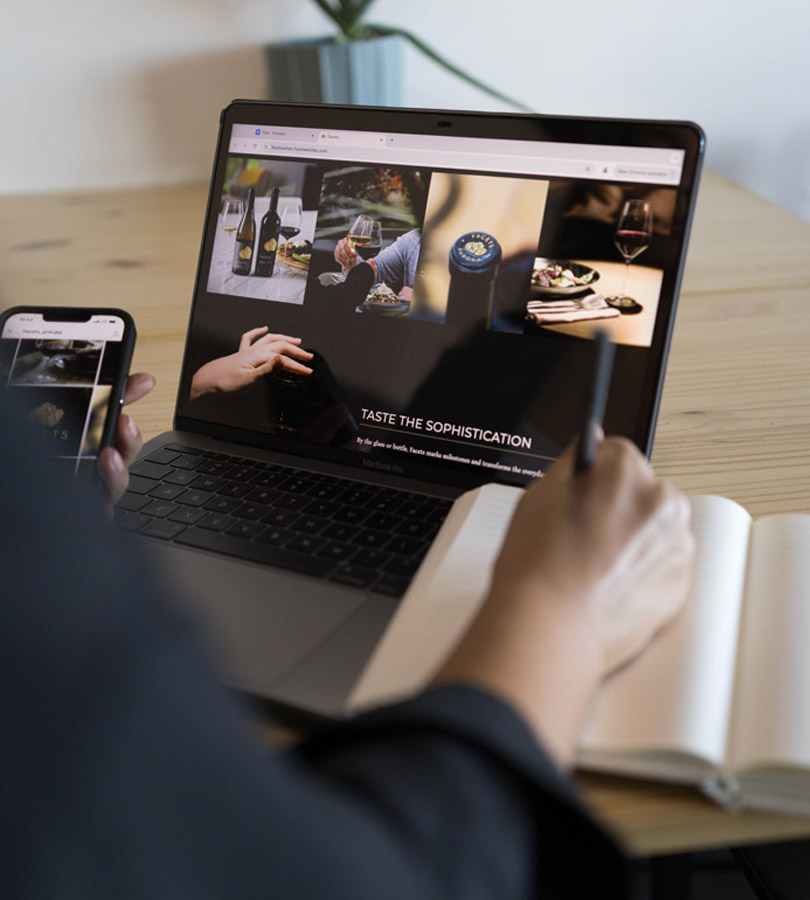 Person using laptop and phone exploring wine products.