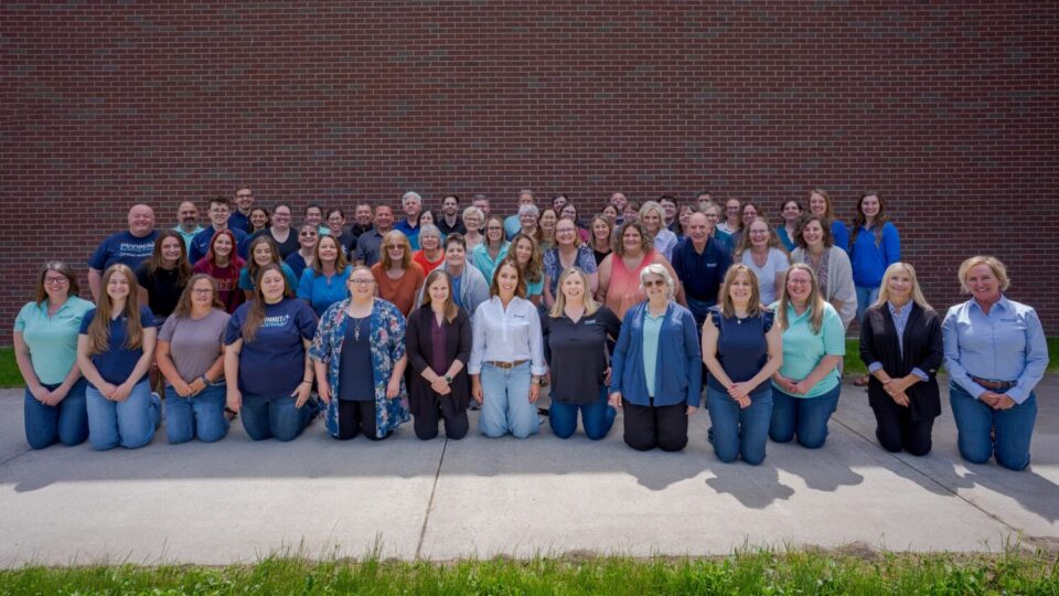 Large group of employees posing outdoors against brick wall