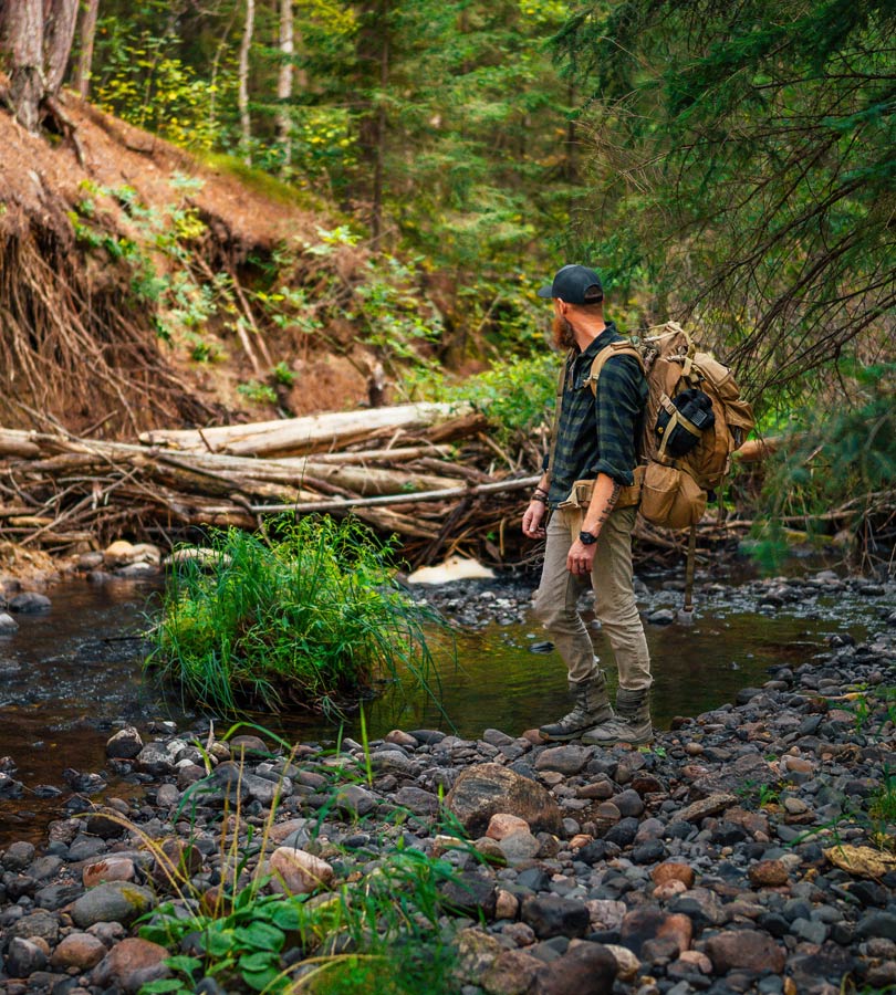 Hiker with backpack crossing a rocky stream in forest.